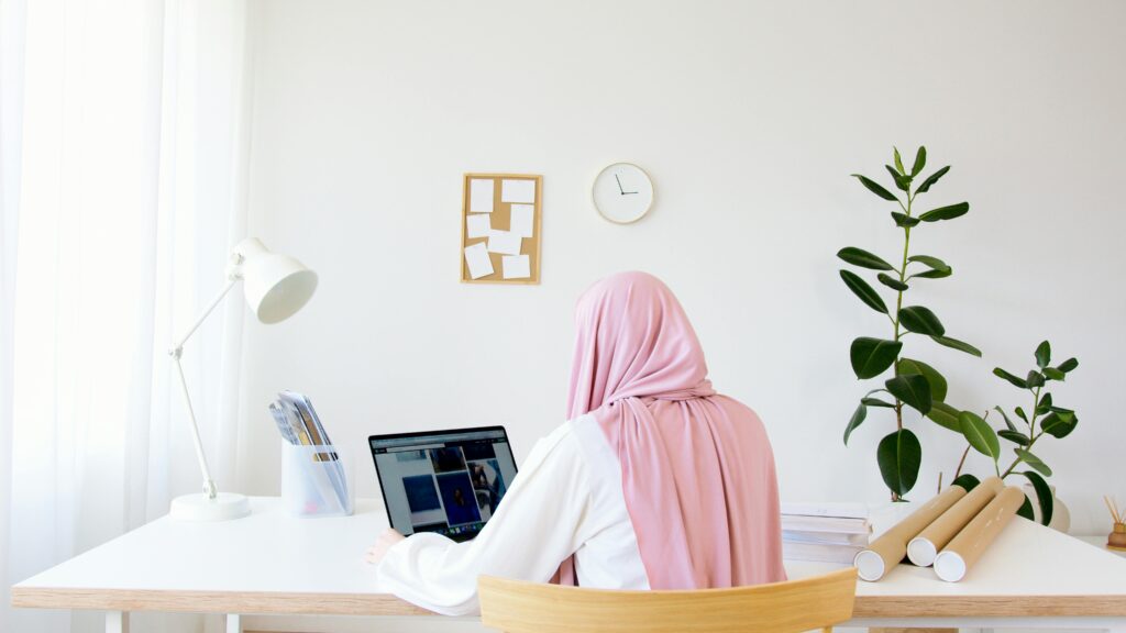 A Muslim woman in a hijab working on a laptop in a modern, minimalist office setting.