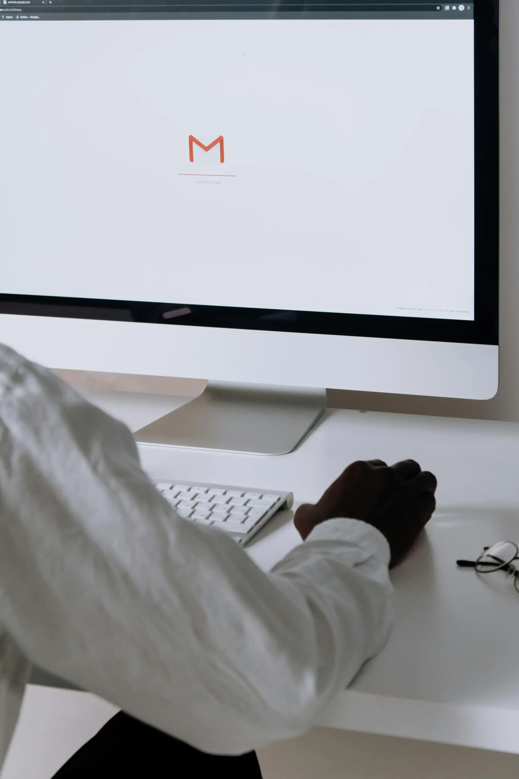 A person wearing white shirt works at a desk with a computer, keyboard and mouse, as seen from a laptop screen displaying email